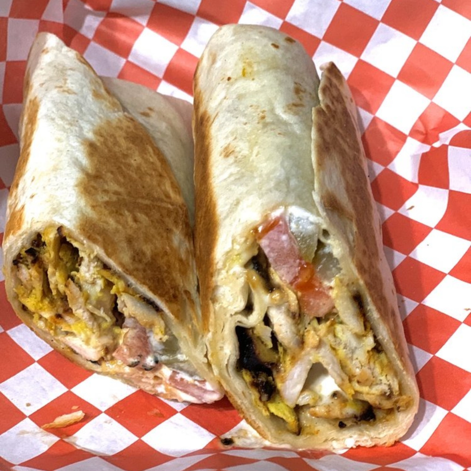 Two halves of a Gyro Grill KC chicken shawarma wrap with vegetables in red and white checkered paper.