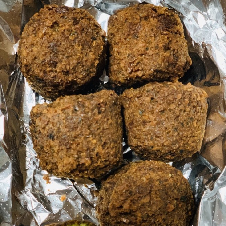 Five golden-brown falafel pieces, a Mediterranean dish, resting in crinkled aluminum foil.