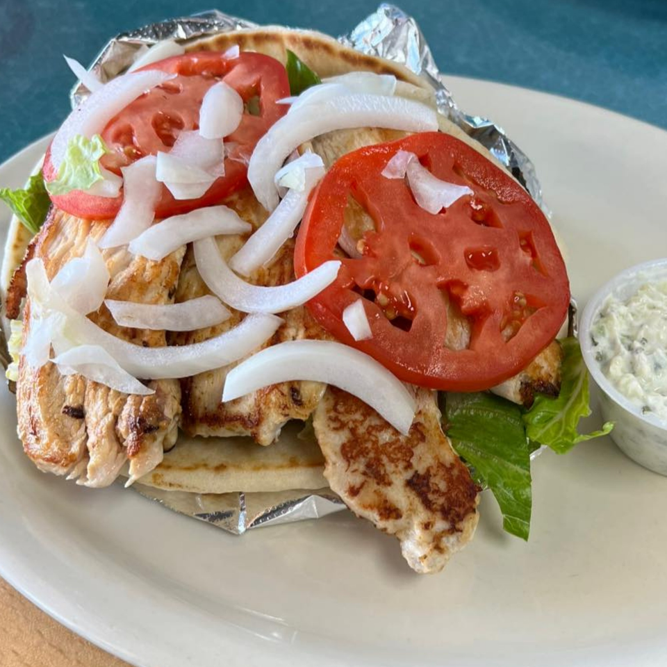 Chicken gyro with tomatoes, onions, and lettuce on pita bread, served with a side of tzatziki.