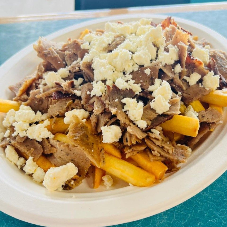 Gyro meat and golden fries topped with crumbled feta cheese on a white plate.